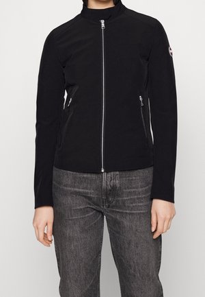 Black zip-up jacket with a high collar and side zip pockets worn with faded black jeans, shown from neck to hips.