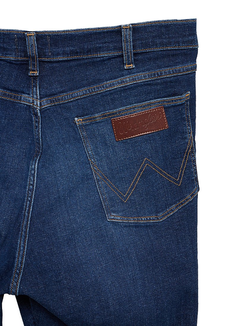 Ciemnoniebieskie dżinsy z brązową skórzaną łatą na tylnej kieszeni, z kontrastującymi żółtymi szwami i klasycznym pięciokieszeniowym fasonem.