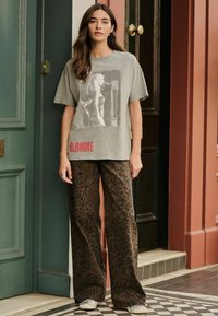 Grå bomulds t-shirt med grafisk print og rød "BLONDIE" tekst, parret med brune leopard-mønstrede brede bukser. Casual stil.