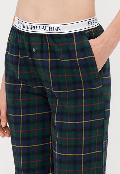 Zaļi un tumši zili rakstotie pidžamu bikses ar baltu jostu, uz kuras ir „Polo Ralph Lauren” logs, sānu kabata un pogu detaļa.