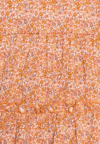 Květinová látka v odstínech oranžové a růžové zdobí jemný vzor květin a listů. Na nařasených částech jsou ozdobné volánky.