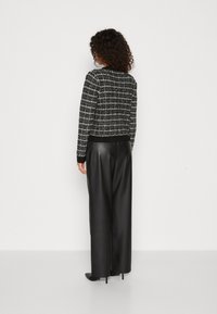 Giacca in tweed bianco e nero con maniche lunghe, tessuto texturizzato e design aderente, abbinata a pantaloni in pelle nera a vita alta.