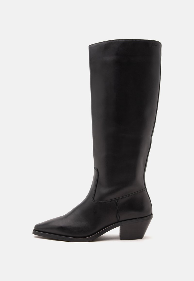 Botte en cuir noire mi-mollet avec un bout pointu et un talon bas incliné sur un fond clair uni.