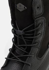Botas negras impermeables con parte superior sintética texturizada, ojales reforzados, cordones negros y un diseño elegante. Presenta un destacado detalle del logo.
