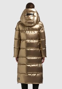 Piumino color oro con finitura lucida, cappuccio, cuciture verticali e zip laterali. Decorato con una patch logo all'orlo.