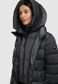 Puffet sort jakke med en oversized hætte, quiltet tekstur, frontlynlås og logo på ærmet. Fremstillet af et blankt materiale.