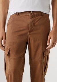 Bruine cargobroek van katoen met een gladde textuur, voorzien van zijzakken, riemlussen en een ritssluiting.