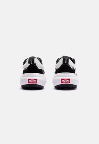 Sneakers in bianco e nero con una parte superiore testurizzata, dotate di una suola intermedia bianca, suola esterna nera e dettaglio del logo Vans rosso sul tallone.