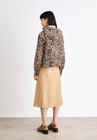Jasje van fleece met luipaardprint en capuchon, gecombineerd met een beige leren midi-rok. Bruine suède schoenen met blokhak maken de outfit compleet.