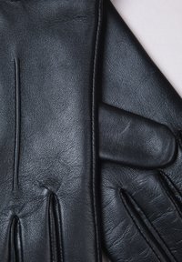 Black leather gloves with a textured finish, featuring four raised seams and a subtle cuff design. Smooth, supple material throughout.