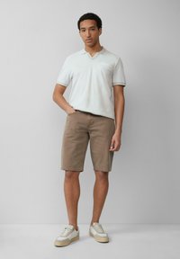 Lichtgekleurde polo met een v-hals en zak, gecombineerd met beige korte broeken. Schoenen hebben een witte leren bovenkant met beige accenten.