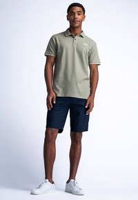 Khakinvärinen pikeepaita, jossa on tekstuuri, yhdistetty tummansinisiin shortseihin. Valkoiset lenkkarit viimeistelevät asun. Yksinkertainen, rento ulkoiluasu.