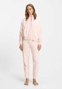 Chaqueta bomber rosa con un patrón texturizado sutil, cierre de cremallera y pantalones a juego. Ambas piezas tienen puños acanalados y un ajuste relajado.