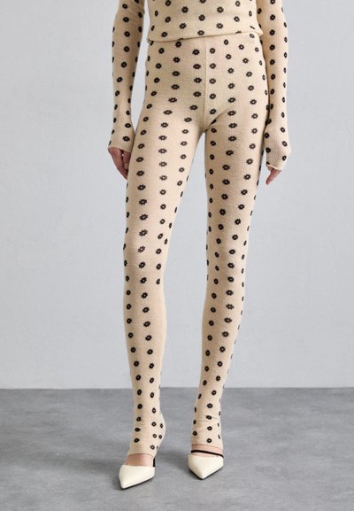 Leggings bej cu model floral negru, cu un design cu nervuri, asortați cu pantofi cu toc alb ascuțit. Prezintă mâneci lungi și un design ajustat.