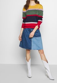 Maglione lavorato a maglia multicolore con righe orizzontali, abbinato a una gonne A-line in denim blu. Il modello indossa stivali bianchi a punta.