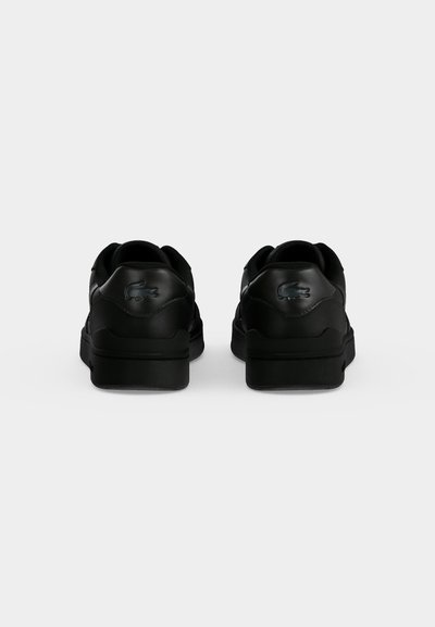 Paire de baskets noires Lacoste vues de dos, avec le logo crocodile embossé sur la languette du talon.