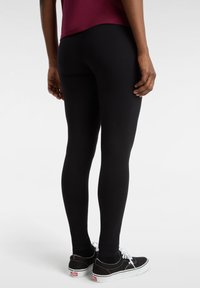 Leggings neri realizzati in tessuto elasticizzato, con una vestibilità slim e vita media, abbinati a sneaker nere basse con accenti bianchi.