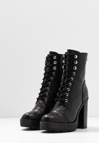 Czarne botki do kostki o fakturze krokodylej, z wiązaniem, srebrnymi oczkami i masywnym wysokim obcasem.