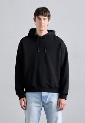 Black hoodie with a relaxed fit, featuring a kangaroo pocket and subtle logo detail. Paired with light blue denim jeans.