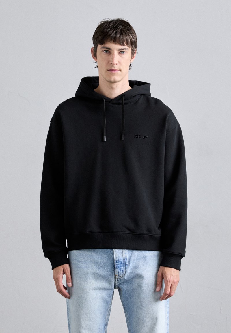 Black hoodie with a relaxed fit, featuring a kangaroo pocket and subtle logo detail. Paired with light blue denim jeans.