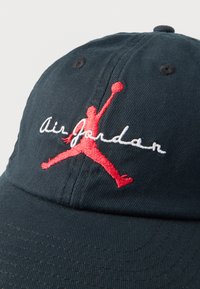 Σκούφος σκούρο μπλε φτιαγμένος από βαμβάκι με κόκκινο κεντημένο λογότυπο Jumpman και λευκό κείμενο «Air Jordan». Διαθέτει καμπυλωτό γείσο και υφή υφάσματος.