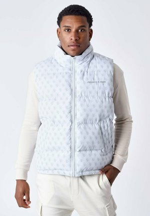 Lichtgrijze puffer vest met een all-over logo patroon, ritssluiting, hoge kraag en zijzakken. Gedragen over een crèmekleurig longsleeve shirt.