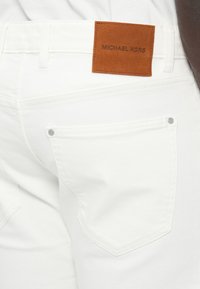 Λευκά τζιν denim με καφέ δερμάτινη ετικέτα που γράφει "MICHAEL KORS." Διαθέτουν τυπική πίσω τσέπη με ασημί εξαρτήματα. Ομαλή υφή.