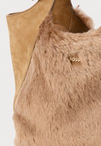 Smeđi nubuk čizmice do gležnja s svijetlosmešavim umjetnim krznom. Ima zlatni akcent s logom "BOSS" i glatku teksturu.