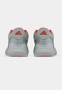 Szürke sportcipők piros részletekkel, texturált felsőrésszel, réteges kialakítással a sarkán és gumitalppal, amelyen látható tapadásmintázatok találhatók.