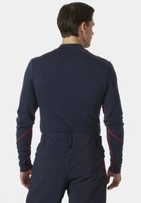 Marineblauw langemouwen top met rode naadaccenten, gemaakt van zacht materiaal. Heeft een aansluitend ontwerp met een ronde hals en reikt tot de taille.