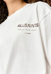 Bílý bavlněný tričko s potištěným logem "ALLSAINTS" v černé a hnědé barvě, s japonským textem a "LONDON" ve spodní části.
