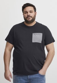 Sort kortærmet t-shirt med en grå lomme på venstre bryst. Lavet af blødt materiale, med en rund halsudskæring og en afslappet pasform.