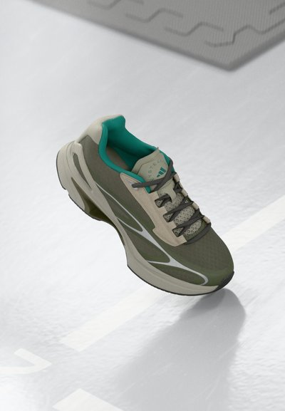 Chaussure de course athlétique verte et beige avec des lacets foncés et une doublure intérieure teal reposant sur une surface de piste intérieure blanche.