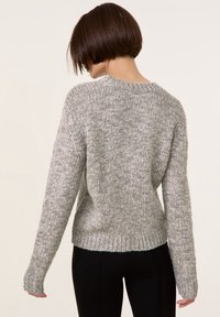Grå strikket sweater med rund halsudskæring, sænkede skuldre og ribbede manchetter. Teksturen er kraftig med et subtilt blandet fiber mønster.