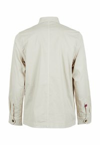 Camicia beige a maniche lunghe con colletto bottonato, caratterizzata da una texture liscia, polsini regolabili e una piccola etichetta con logo sulla cucitura laterale.