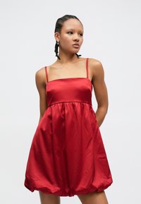 Rochie roșie din satin cu bretele subțiri, corset strâmt și fustă evazată, ușor adunată. Textură fină, lungime peste genunchi.