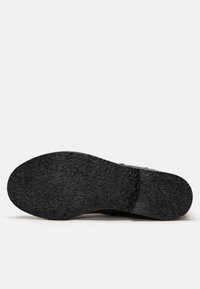 Suela de zapato de goma negra con superficie texturizada, forma redondeada y marcas en relieve. Sin señales visibles de desgaste ni patrones.