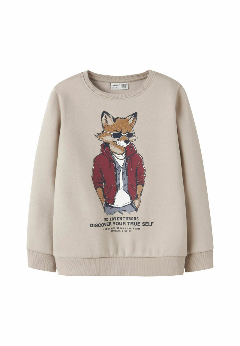 Bež sweatshirt s grafikom lisice u naočalama i crvenoj jakni, s natpisom "Budi avanturističan, otkrij svoju pravu prirodu" ispod.