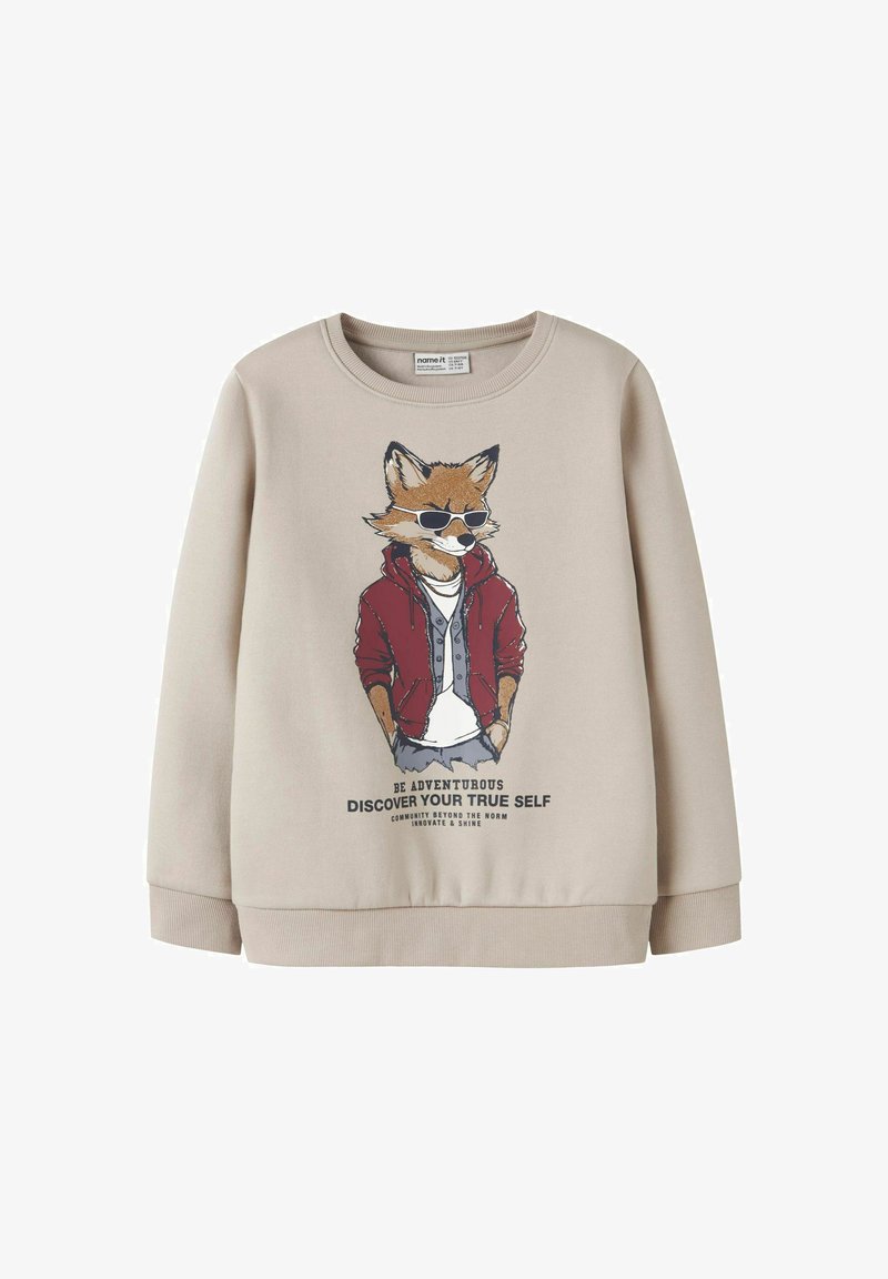 Bež sweatshirt s grafikom lisice u naočalama i crvenoj jakni, s natpisom "Budi avanturističan, otkrij svoju pravu prirodu" ispod.