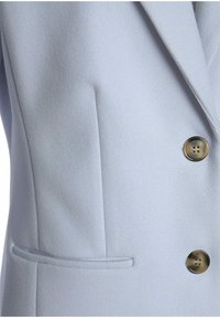 Ljusblå ullblazer med notchad krage, en bröstficka och guldtonade knappar med fyra hål. Slät textur och skräddarsydd design.