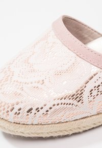 Pantoufle à motifs rose et or rose avec une tige en textile doux, une forme ronde et une semelle en jute naturel. Mise en valeur par une bordure en daim.