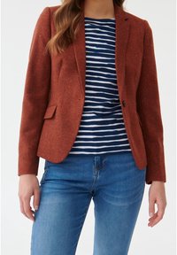 Blazer marron texturé avec un seul bouton et deux poches avant, porté sur une chemise à rayures bleues et blanches, associé à un jean bleu.
