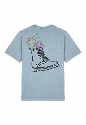 T-shirt bleu clair avec une silhouette noire d'une botte remplie de fleurs colorées, comprenant des fleurs roses et violettes, dans le dos.