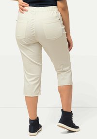 Beige croptrousers met een rafelige zoom, voorzien van twee achterzakken, een elastische tailleband en gecombineerd met marineblauwe high-top sneakers.