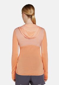 Camiseta atlética ligera de manga larga en tejido naranja degradado. Con capucha, paneles texturizados y agujeros para los pulgares en los puños.