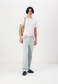 Jeans en denim bleu clair avec une coupe droite, associés à un t-shirt blanc uni et des baskets navy. Un sac à bandoulière beige est porté.