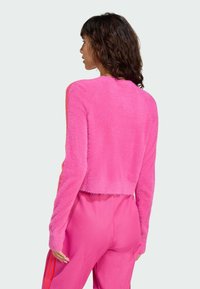 Fuzzy pink cropped sweater with long sleeves, soft texture, round neckline, and a straight hem, paired with pink athletic pants featuring stripes.