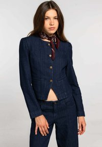 Chaqueta de mezclilla oscura con un diseño corto, acentuada con botones dorados y bolsillos de parche. Combinada con pantalones de mezclilla oscura a juego.