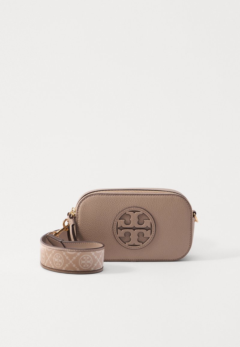 Brown leather crossbody bag with a textured finish, circular logo detail, and an adjustable strap featuring a logo pattern.