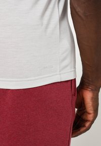 Kortärmad vit T-shirt i lätt tyg, med rundad halsringning och en liten "CLIMALITE"-etikett vid fållen, kombinerad med röda byxor.